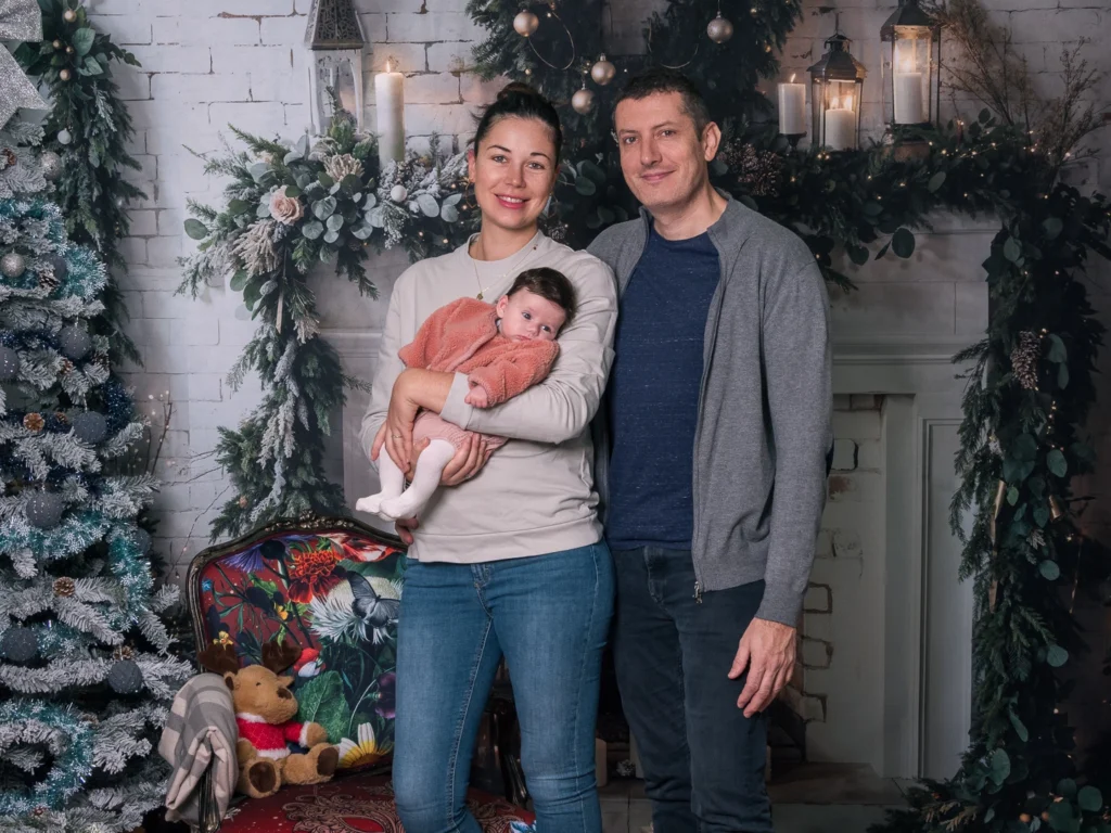Parents et bébé devant le sapin et la cheminée d’un décor de Noël au Studio Timeless à Limoges