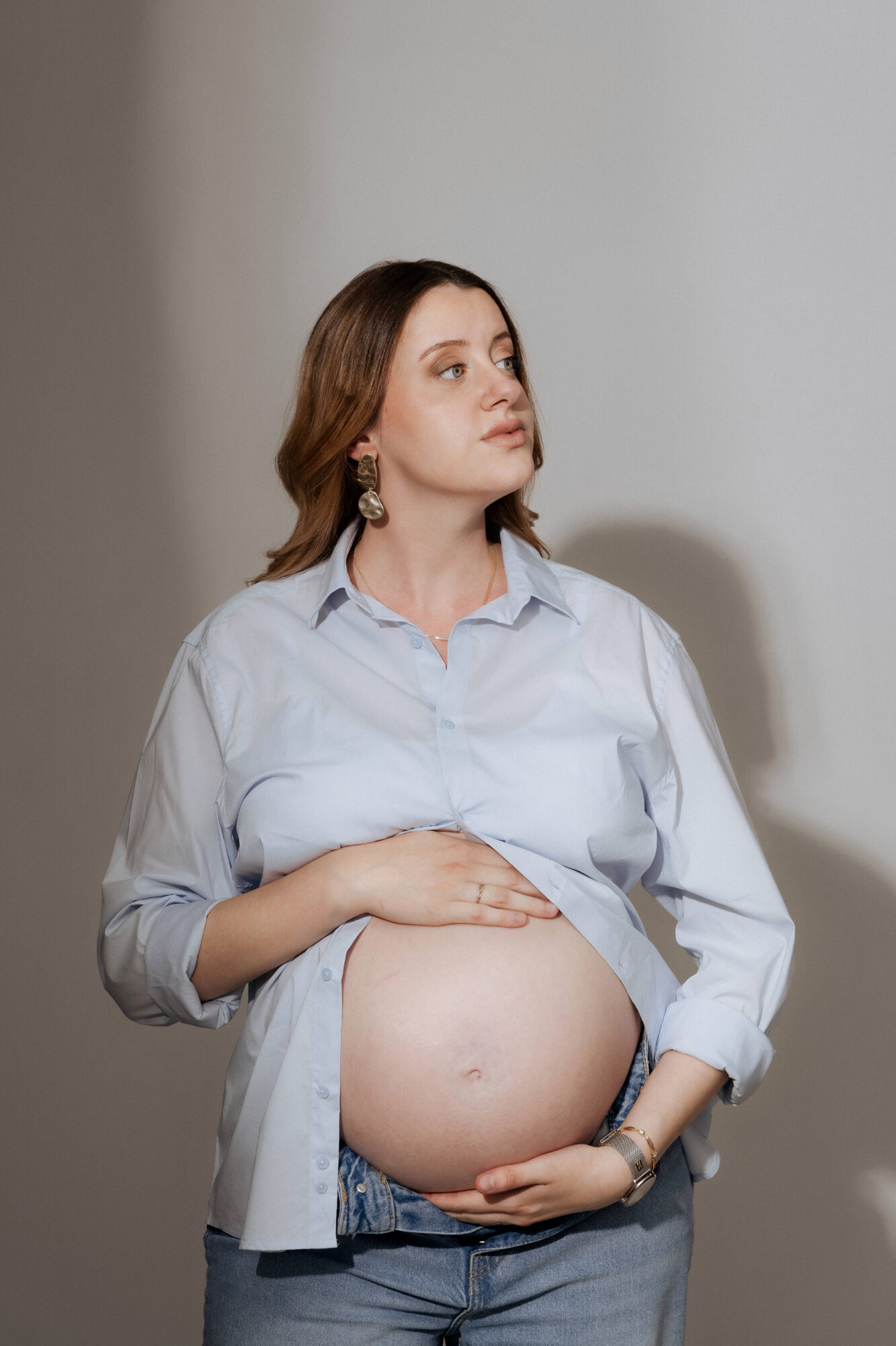 Femme enceinte chemise bleue mains sur ventre fond clair