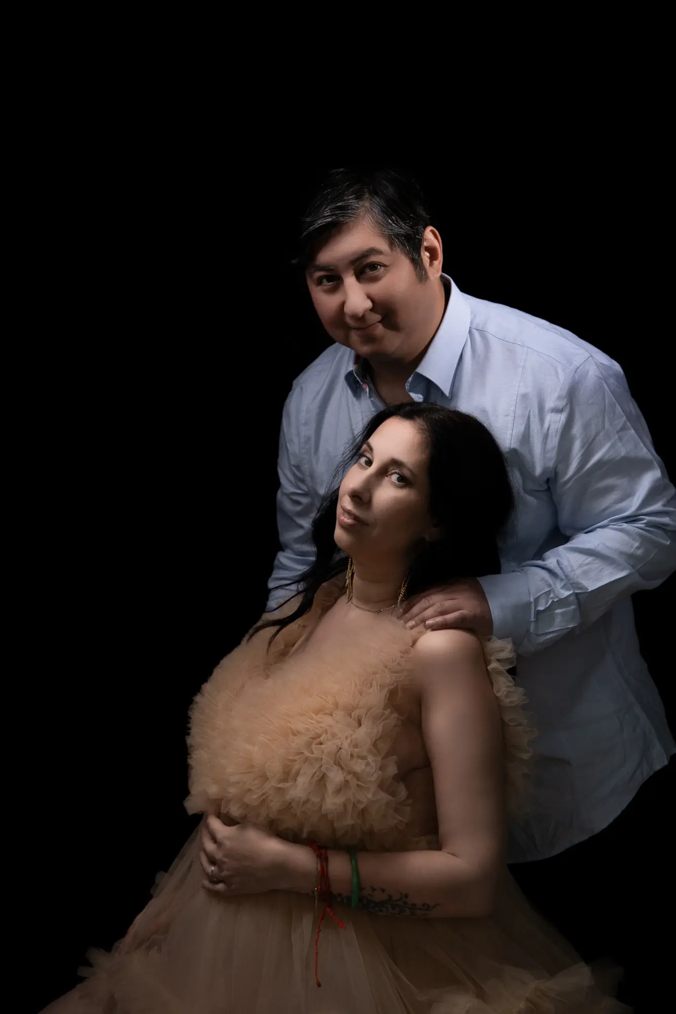 Couple maternité sur fond sombre future maman en robe tulle doré